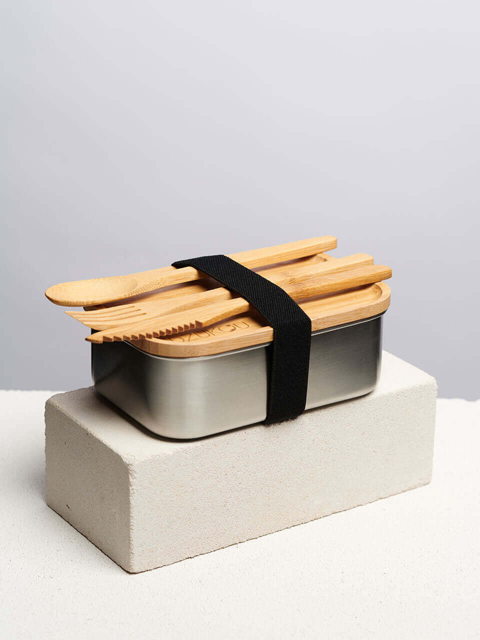 A bamboo lunch box with wooden utensils and cutlery placed on top, showcasing an eco-friendly dining option.