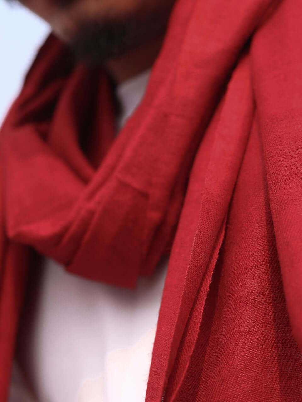 A close-up of a man elegantly wearing a vibrant red scarf, showcasing texture and color against a neutral background.