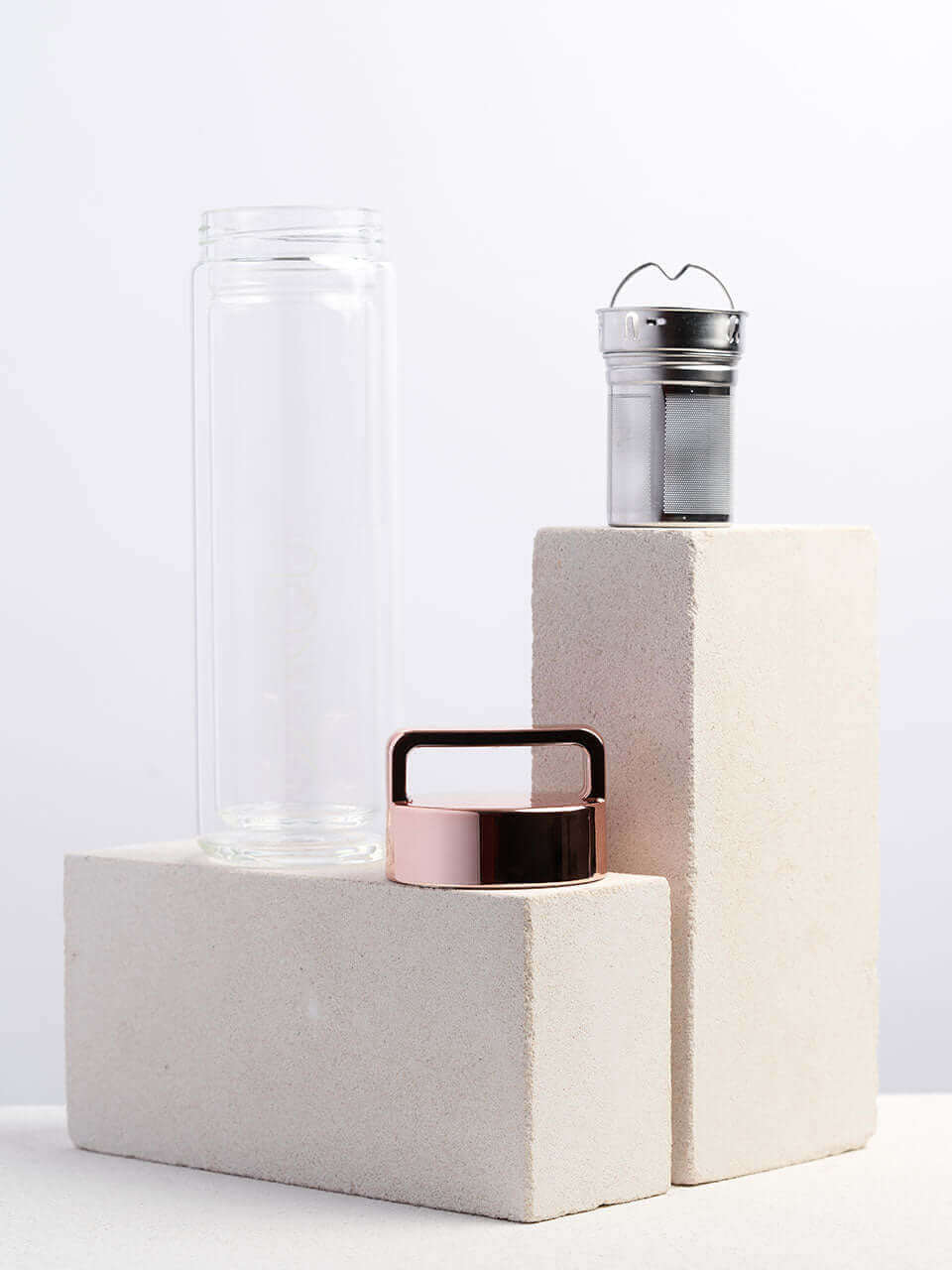 A glass bottle with a lid and a infuser sits atop a white block, showcasing a simple yet elegant storage solution.