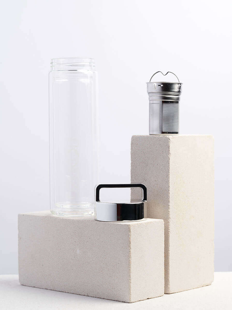 A glass bottle with a lid and a infuser sits atop a white block, showcasing a simple yet elegant storage solution.
