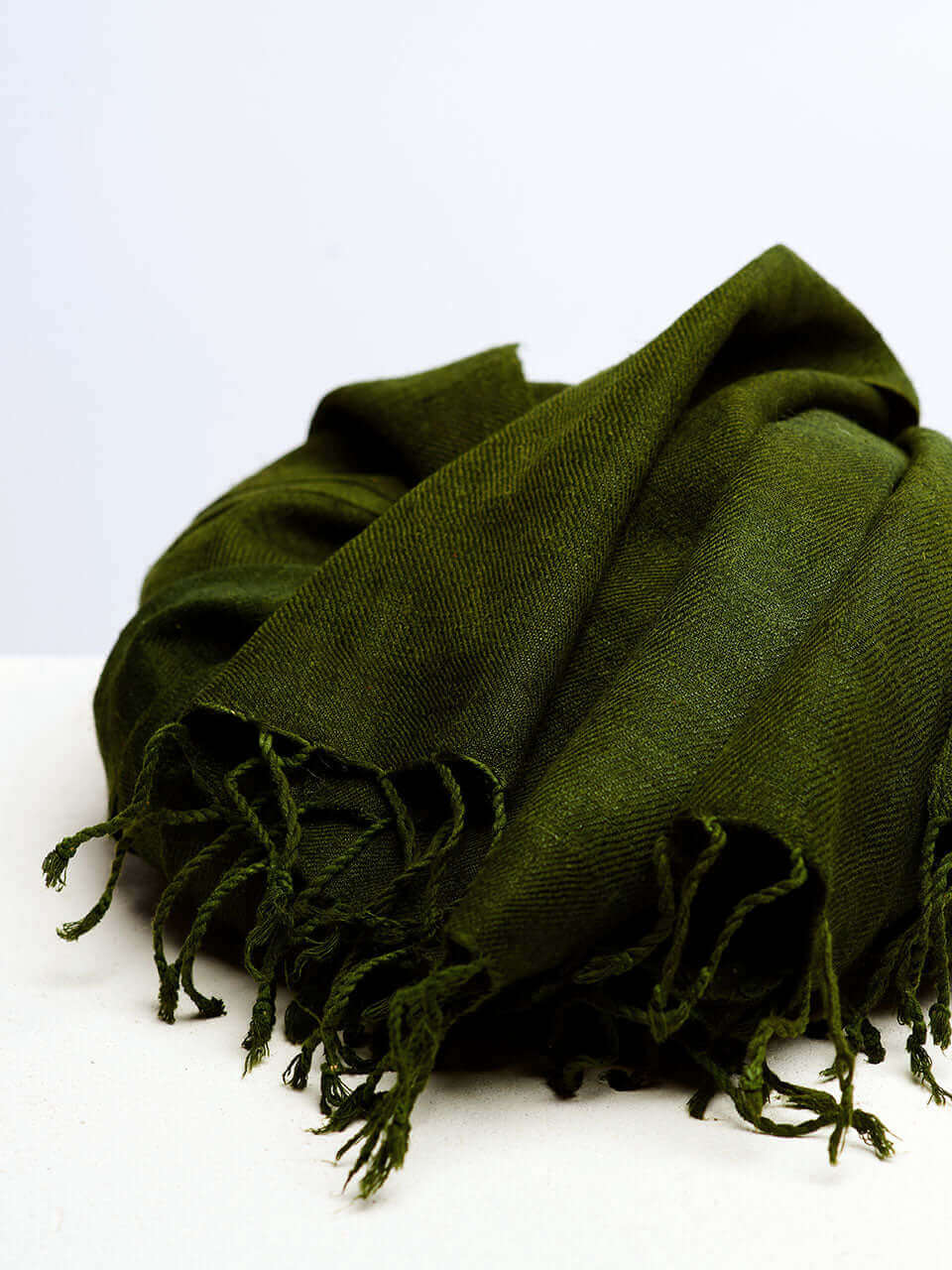 A green scarf resting on a clean white surface, showcasing texture and color contrast.