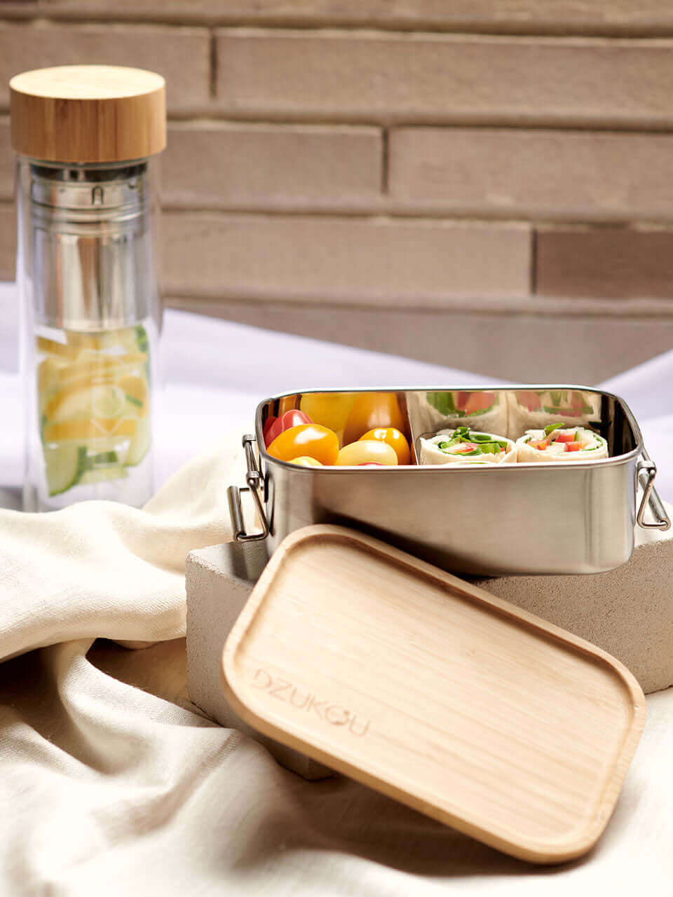 A bamboo lunch box containing waffles and assorted fresh fruit on top of a white block, arranged neatly for a balanced meal.