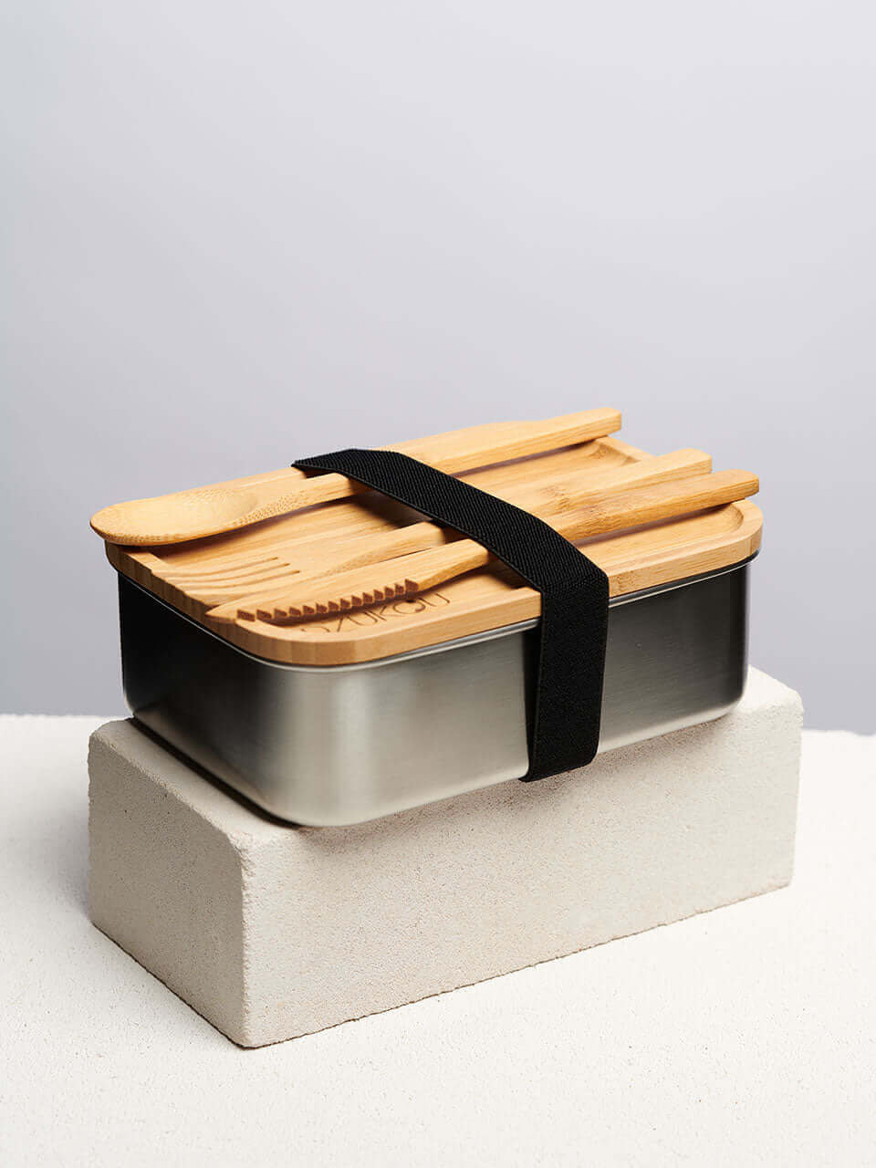 A bamboo lunch box with wooden utensils and cutlery placed on top, showcasing an eco-friendly dining option.