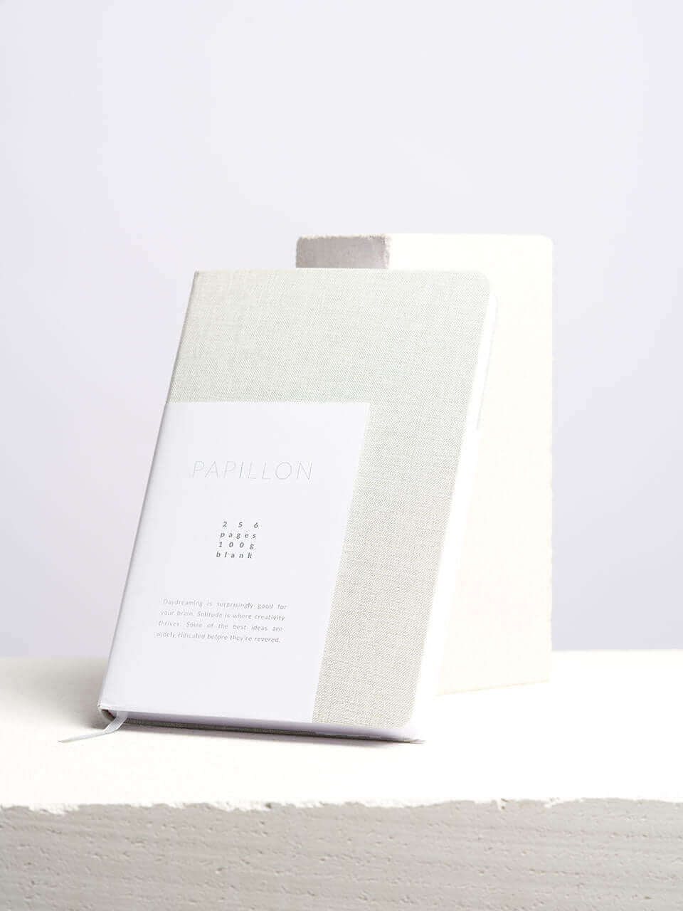 A linen notebook place beside a white block with a clean white background.