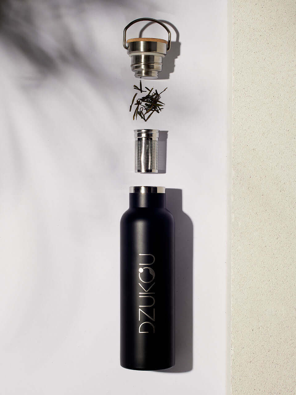 A stainless steel black water bottle with a lid, accompanied by a infuser resting beside it.