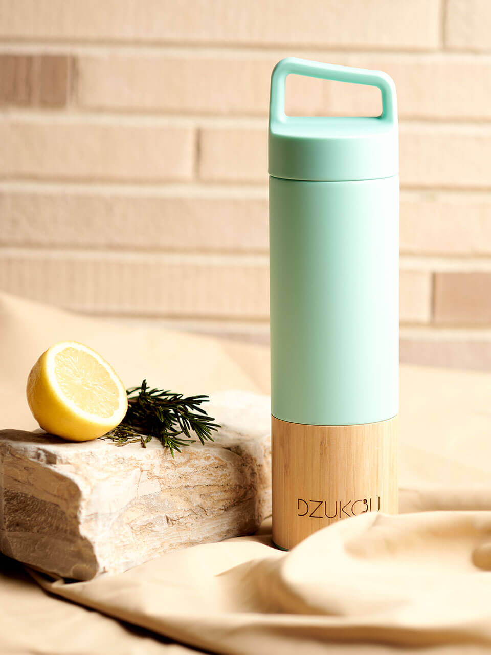 A stainless steel water bottle displayed against a beige background with the lemon and some herbs on the side, highlighting its eco-friendly design.