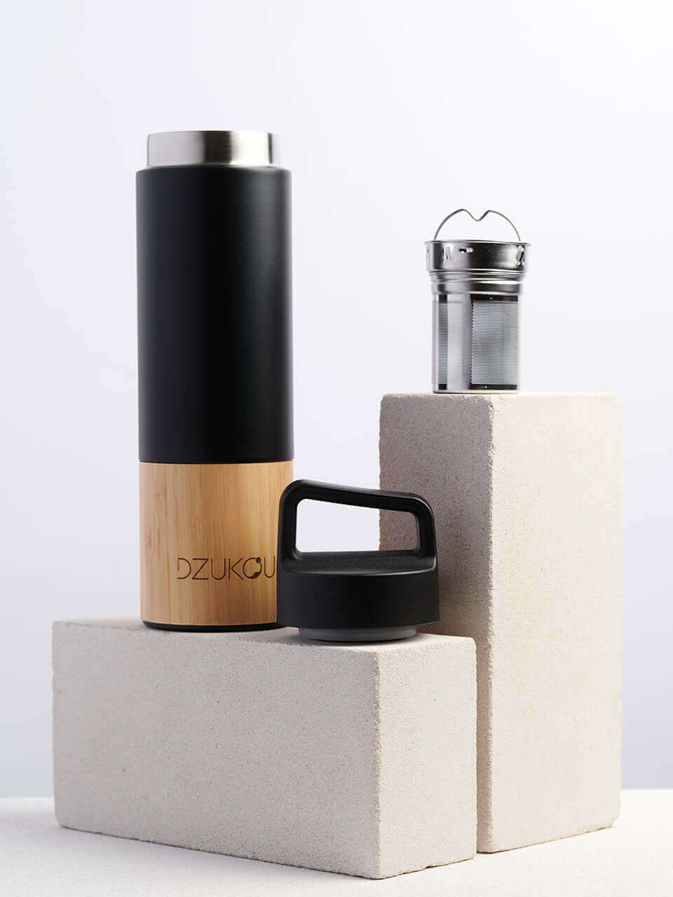 A black and bamboo stainless steel water bottle placed next to a brick on a white background.