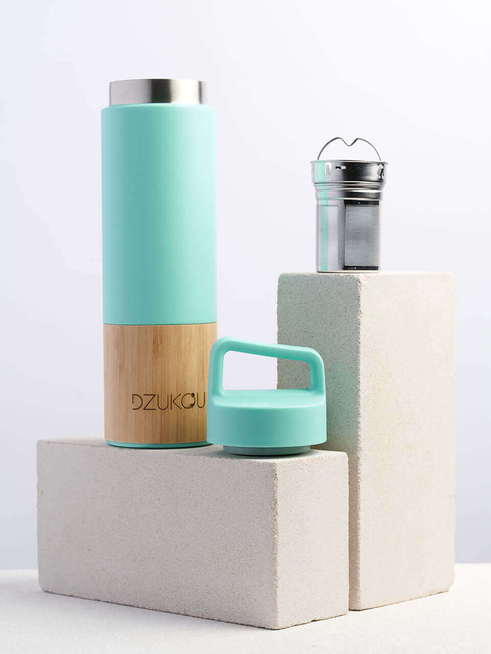 A green and bamboo stainless steel water bottle placed next to a brick on a white background.