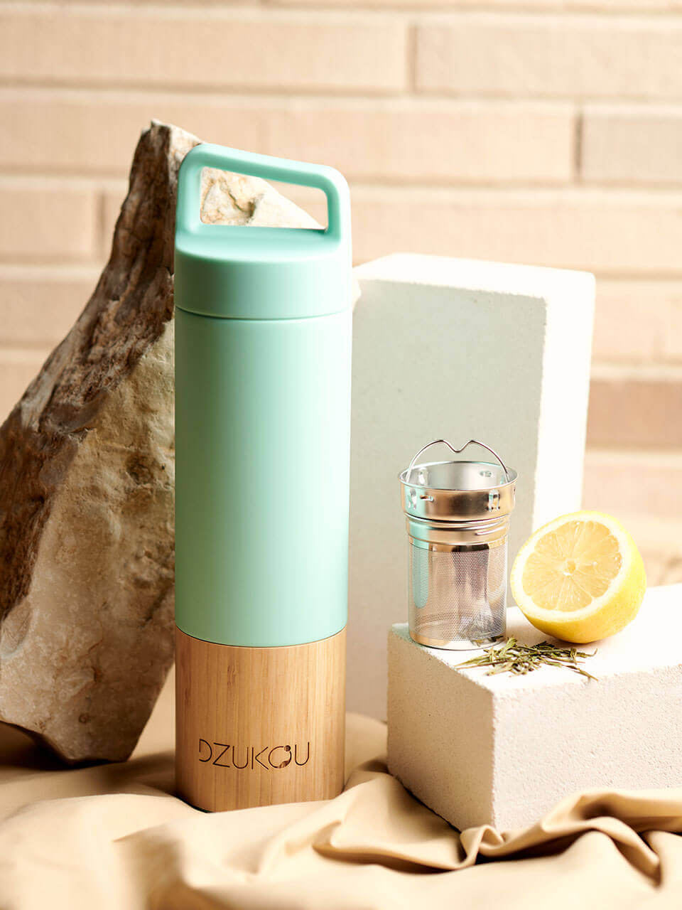 A stainless steel water bottle displayed against a beige background with the infuser on the side, highlighting its eco-friendly design.