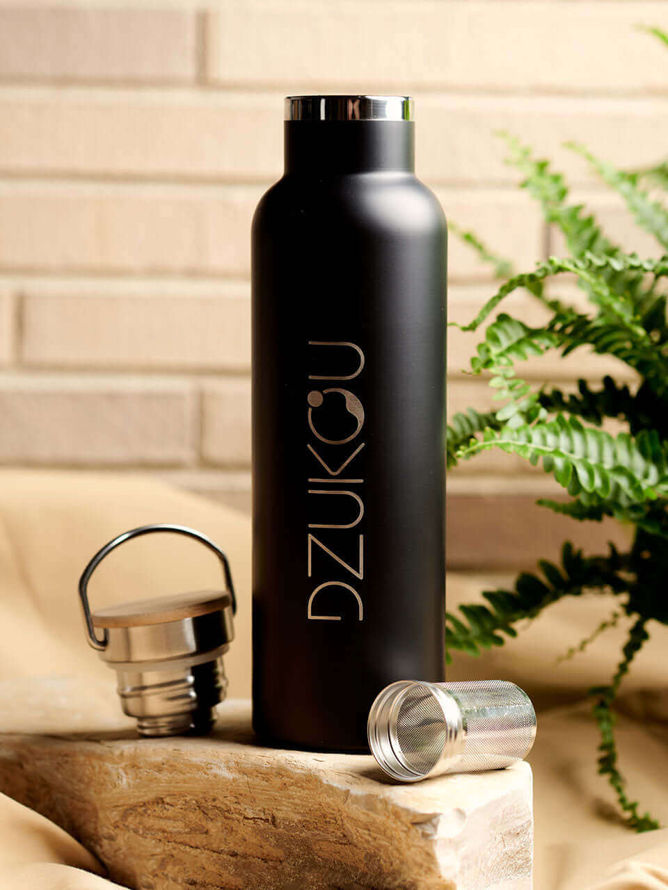 A stainless steel water bottle displayed against a beige background with the infuser and the lid on the side, highlighting its eco-friendly design.