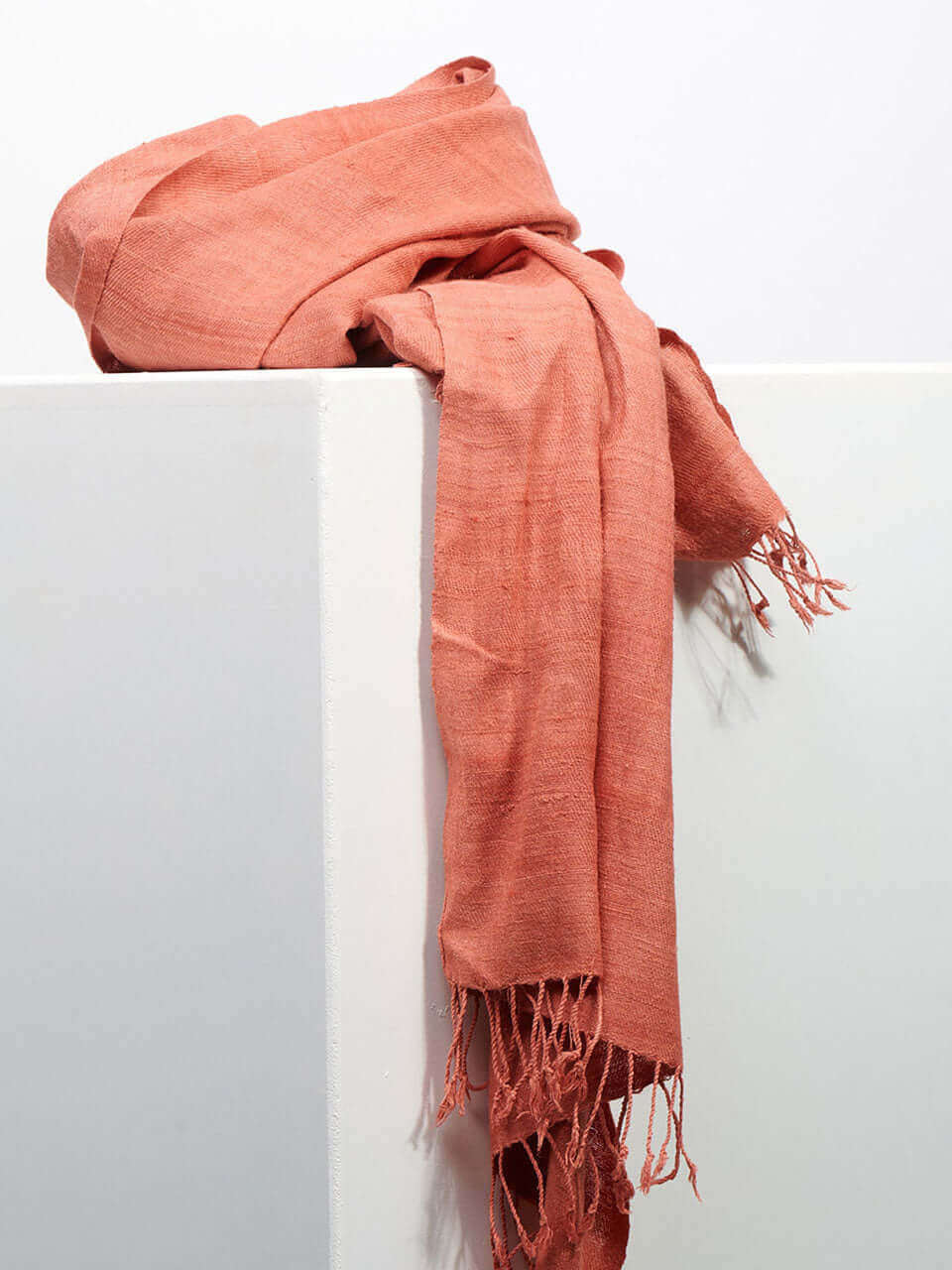 A pink scarf elegantly draped against a clean white wall, creating a soft and vibrant contrast.