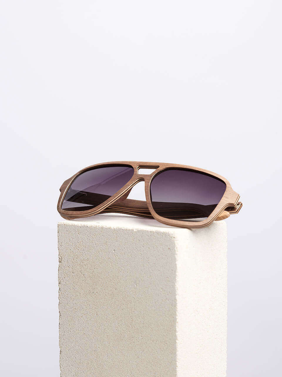 A wooden sunglass resting on a solid block, showcasing their sleek design and reflective lenses.