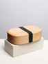 A wooden lunch box featuring a prominent black band wrapped around its exterior.