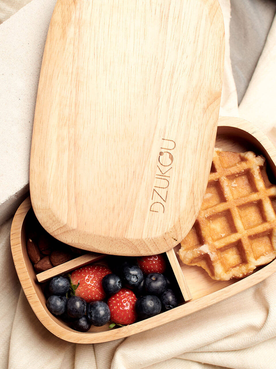 A wooden box with the lid slightly open containing waffles topped with fresh berries.