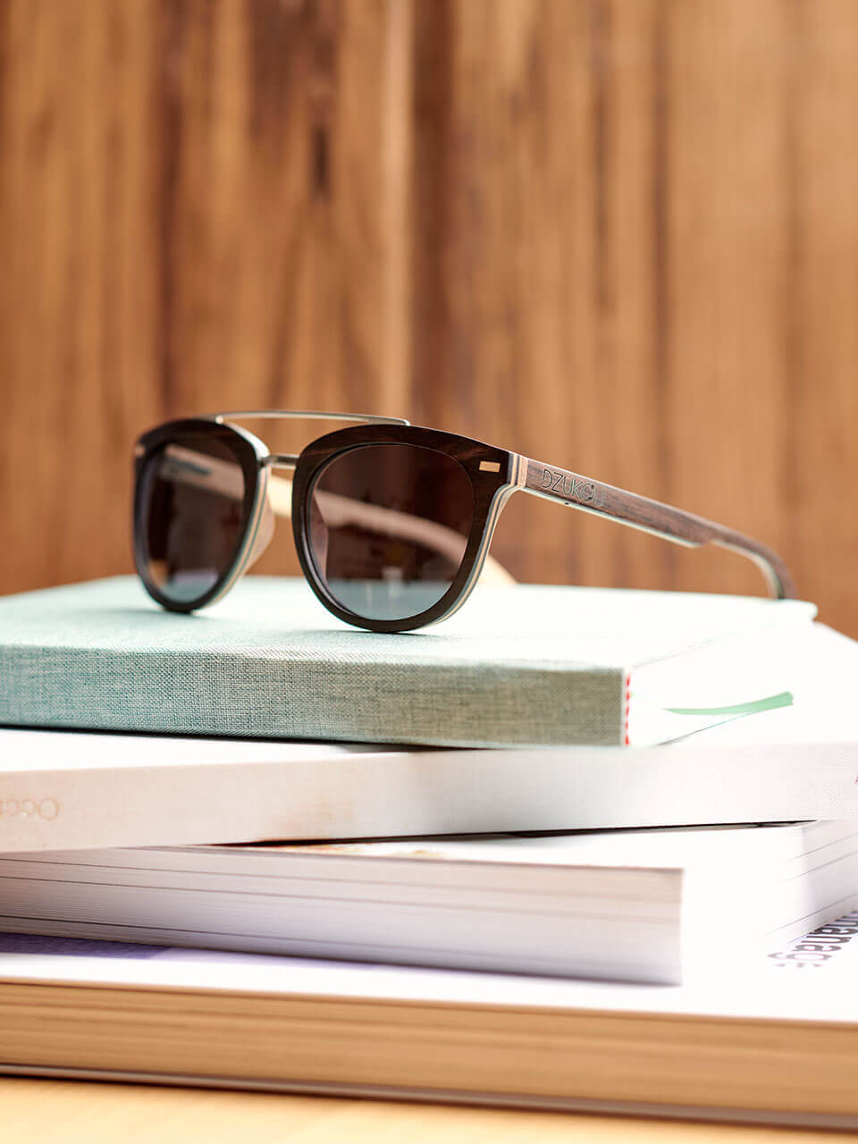 A wooden sunglass rests atop a neatly arranged stack of books, creating a stylish and intellectual aesthetic.