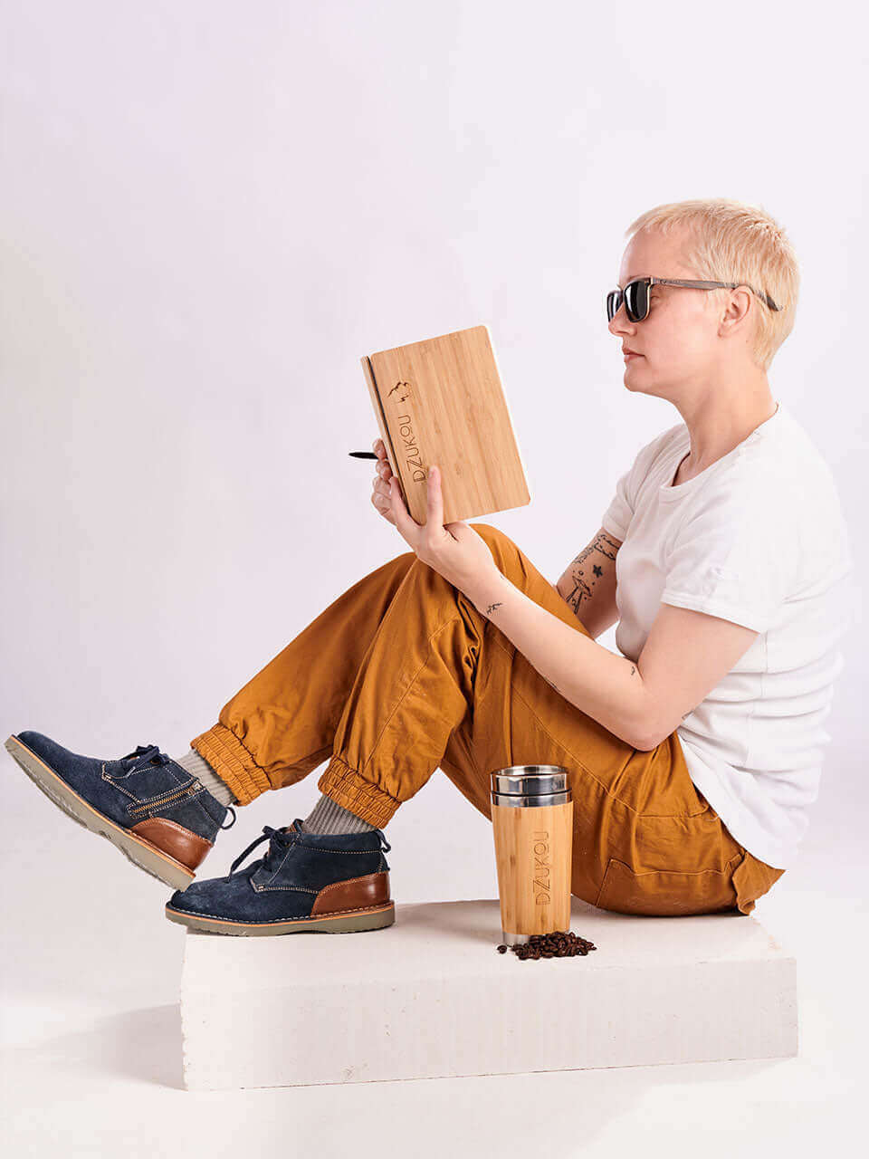 A woman seated on a white clean box, enjoying a book and a cup of coffee in a serene setting.