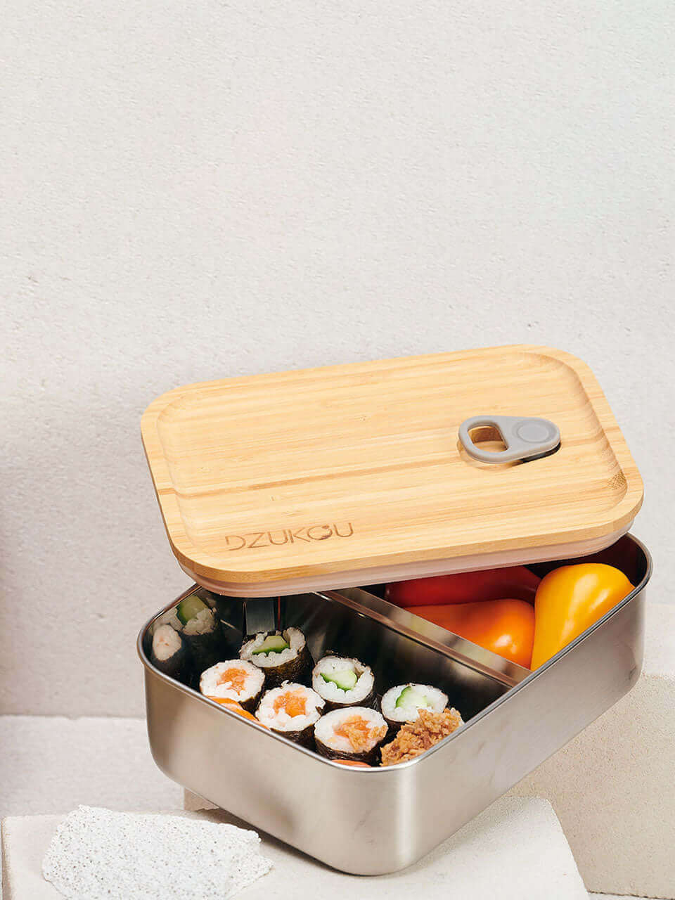 A bamboo lunch box containing sushi and assorted fresh fruit on top of a white block, arranged neatly for a balanced meal.