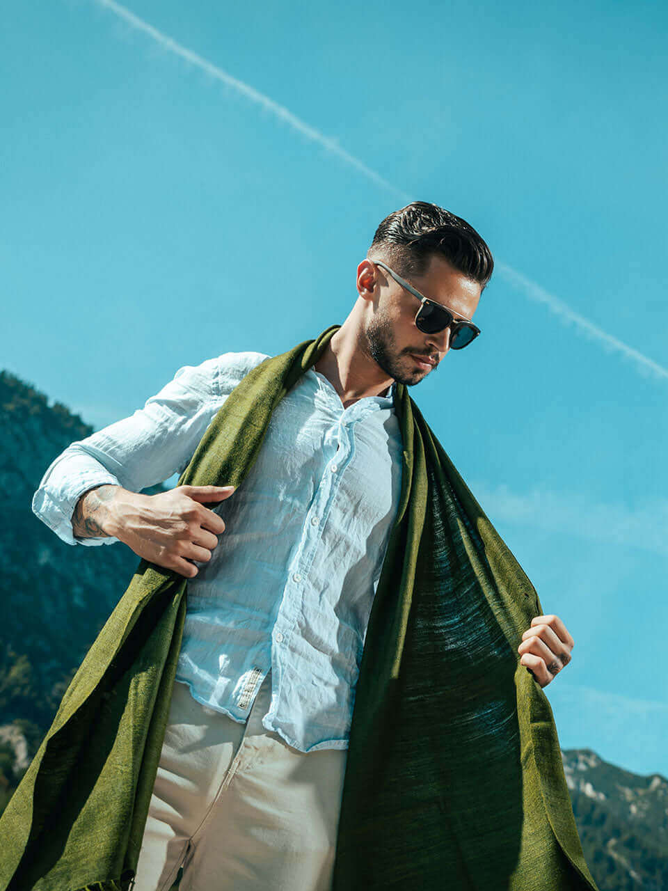 A man wearing a green scarf and sunglasses, exuding a stylish and confident demeanor.