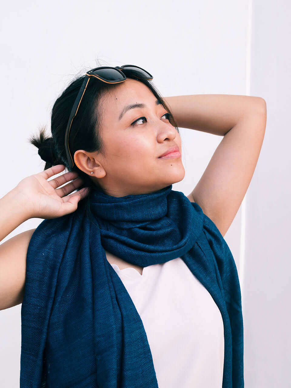 A woman with sunglasses and a blue scarf, exuding elegance and style in a sunny outdoor setting.