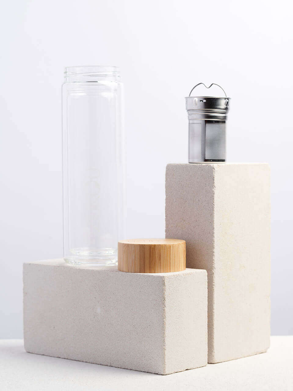 A glass bottle with a lid and a infuser sits atop a white block, showcasing a simple yet elegant storage solution.