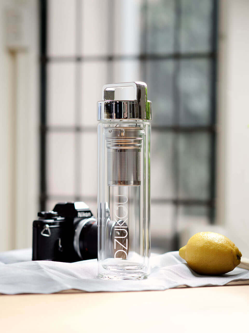 A glass bottle filled with refreshing cucumber pieces with a camera and a lemon on the sides, showcasing a vibrant and healthy beverage.