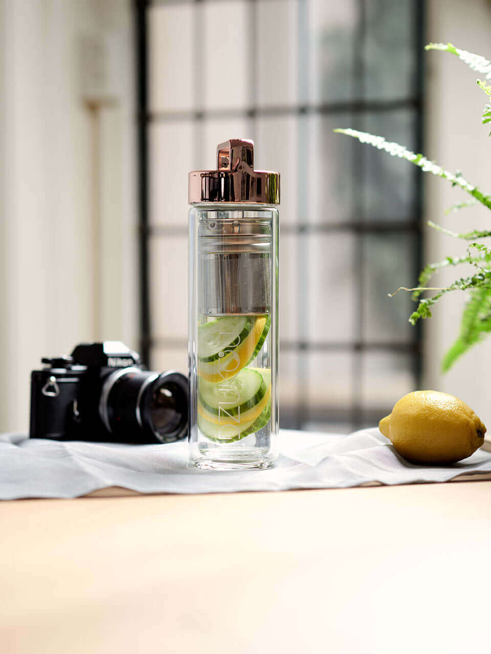 A glass bottle filled with refreshing cucumber pieces with a camera and a lemon on the sides, showcasing a vibrant and healthy beverage.