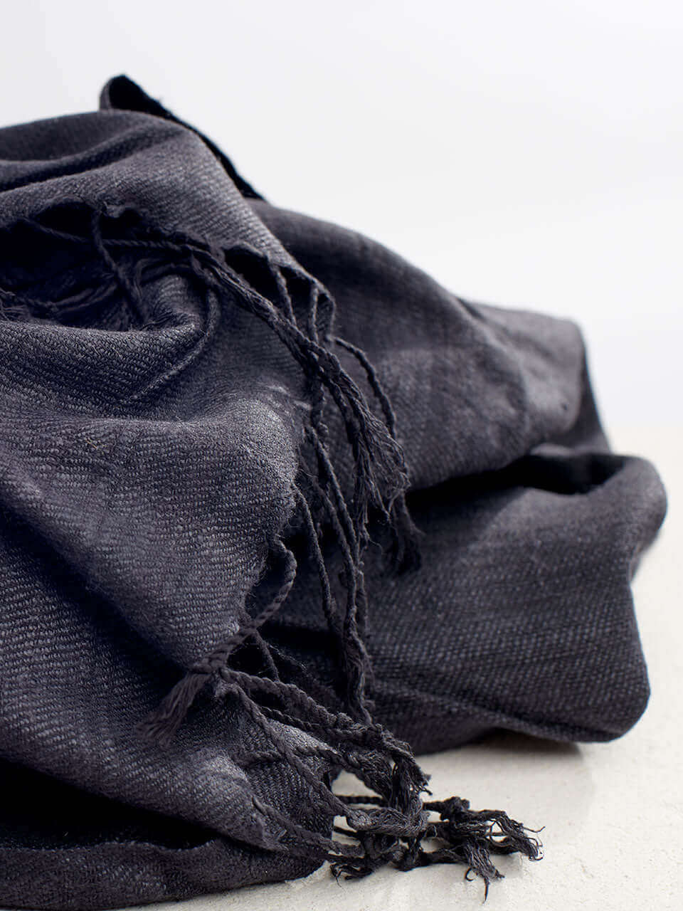 A textured pile of grey scarf featuring decorative fringes, creating a rich and layered appearance.