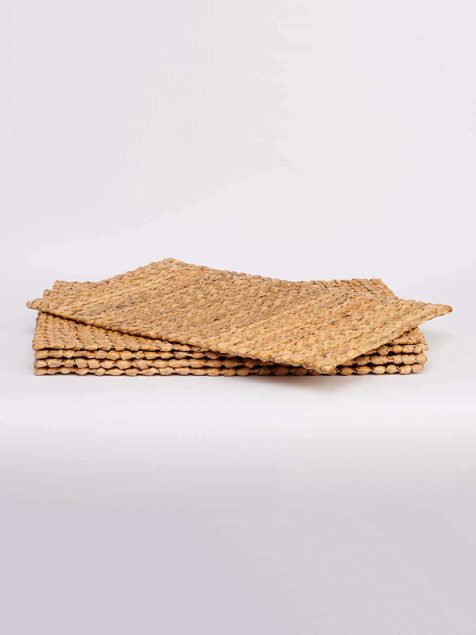 A stack of four water hyacinth placemats pieces arranged neatly on a white background, showcasing their natural texture and color.