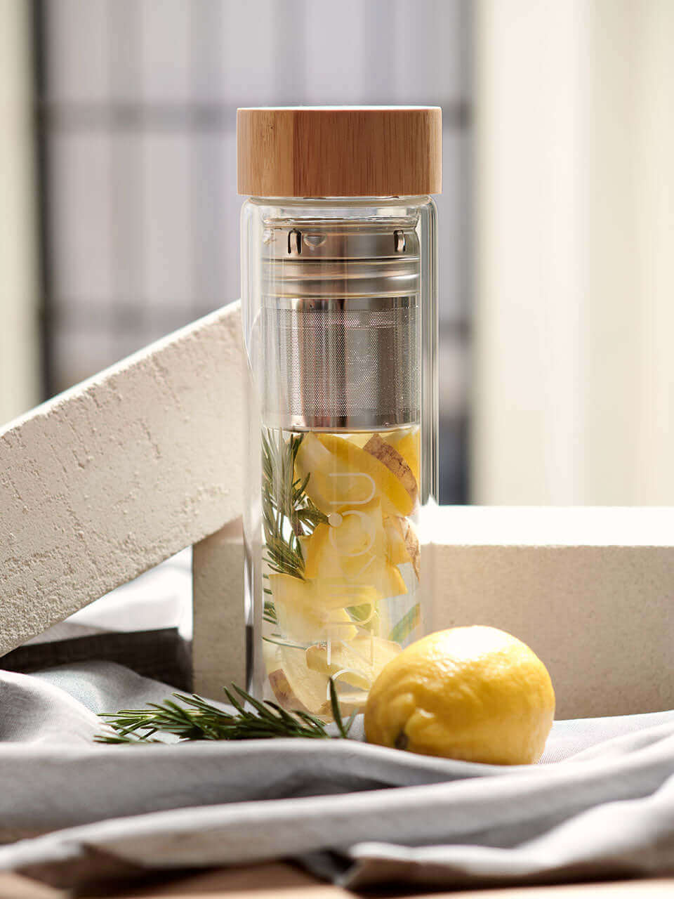 A glass bottle filled with lemon slices and fresh herbs, elegantly placed on a wooden table.