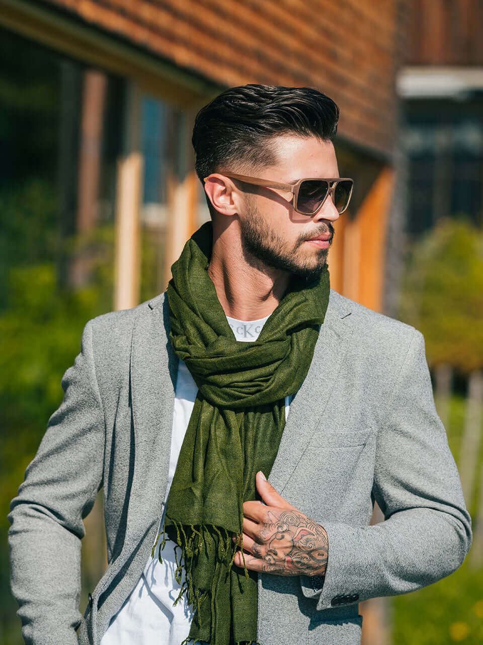 A man in a suit and wooden sunglasses, elegantly styled with a green scarf, exudes confidence and sophistication.