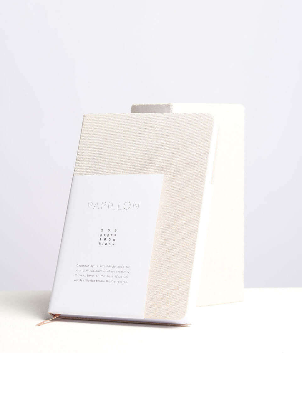 A linen notebook place beside a white block with a clean white background.
