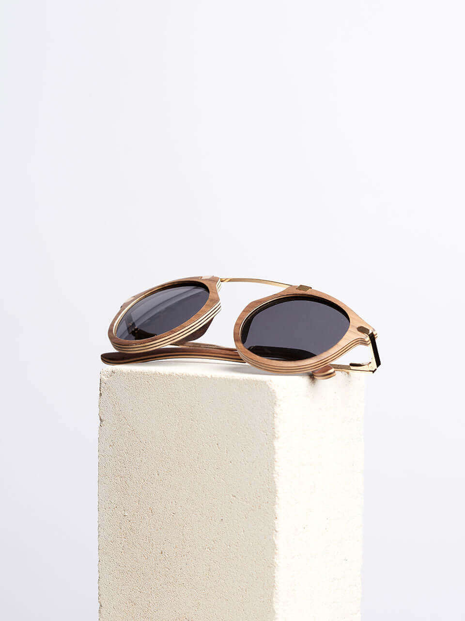 A pair of wooden sunglasses resting on a solid block surface, showcasing their sleek design and reflective lenses.