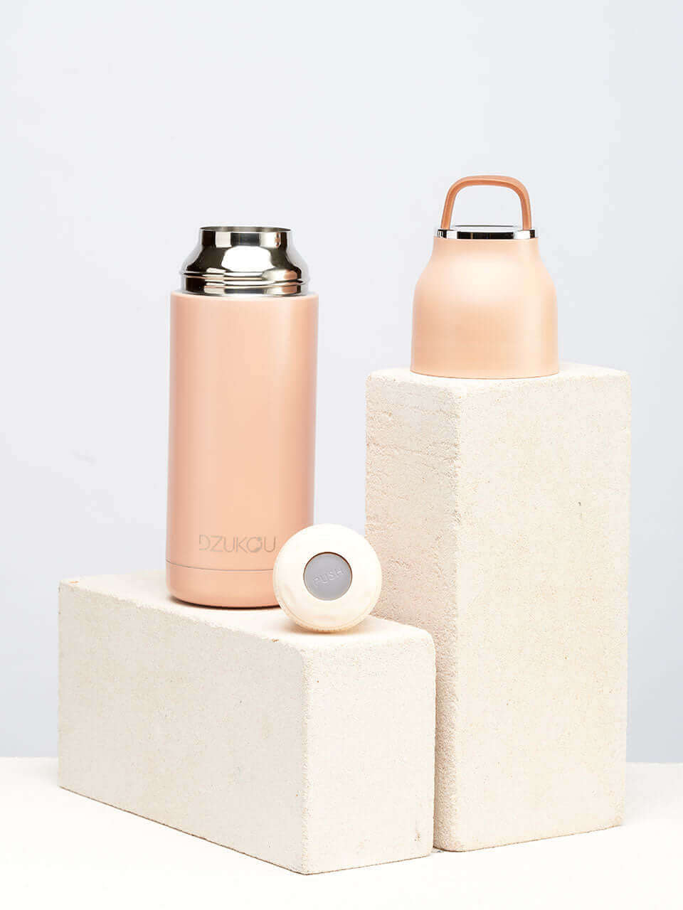A peach stainless steel water bottle placed next to a brick on a white background.