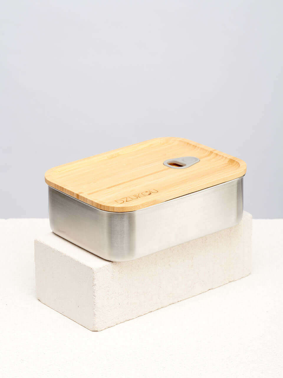 A bamboo lunch box with a vacuum seal on top of a white block, designed for secure storage.