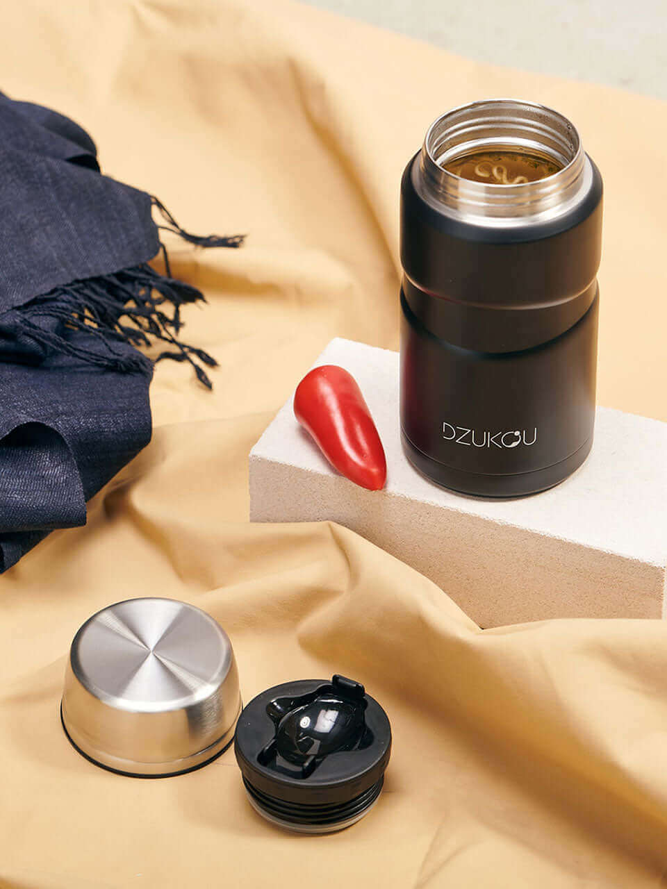 A stainless steel black lunchpot featuring a red pepper and a scarf, showcasing a unique and vibrant design.