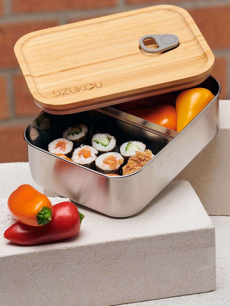 A bamboo lunch box containing sushi and assorted fresh fruit on top of a white block, arranged neatly for a balanced meal.