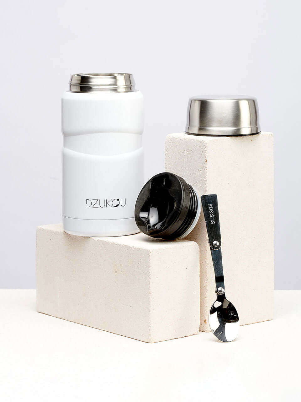 A white lunchpot with a lid and a spoon placed beside it, suitable for storing food or ingredients.