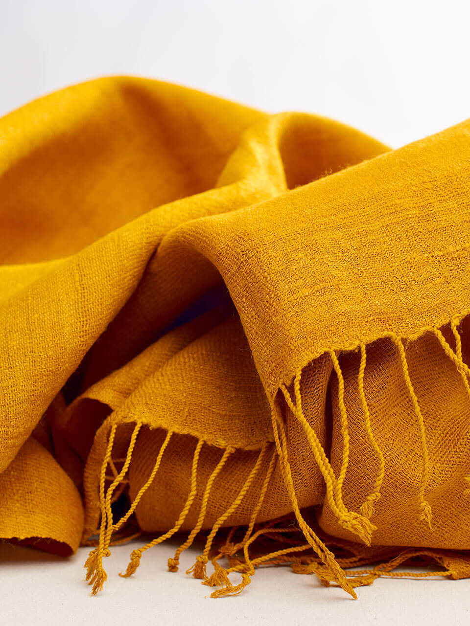 A vibrant yellow scarf adorned with fringes, elegantly draped to showcase its texture and color.
