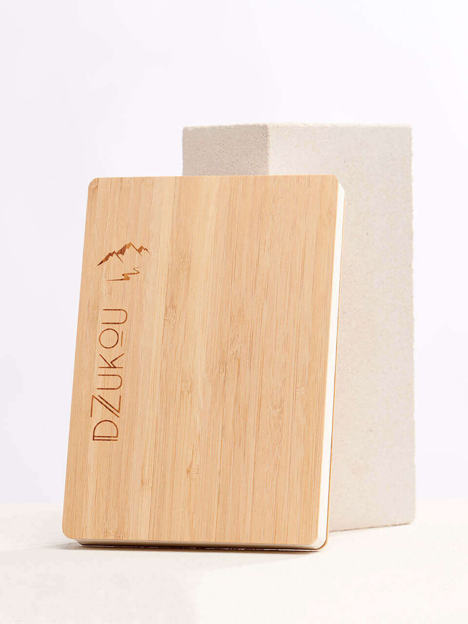 A bamboo notebook placed beside a white block with a clean white background