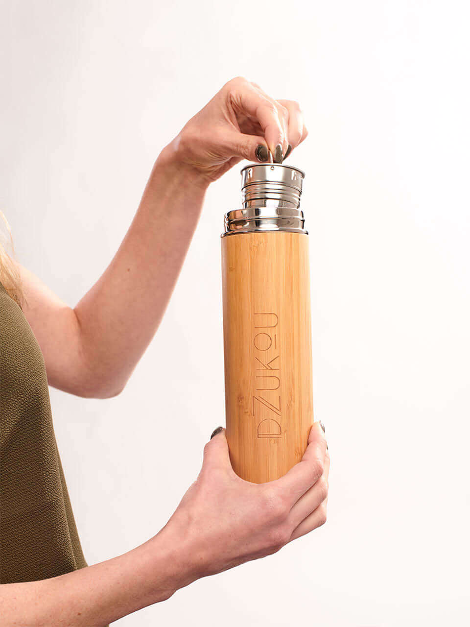 A woman is holding a bamboo water bottle with a lid, showcasing its natural texture and design.
