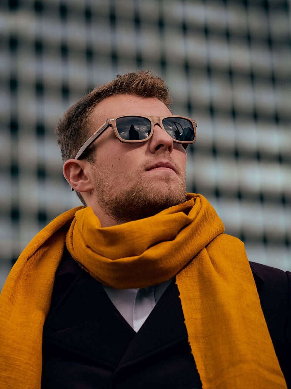 A man wearing a wooden sunglasses and a scarf, exuding a stylish and confident demeanor.