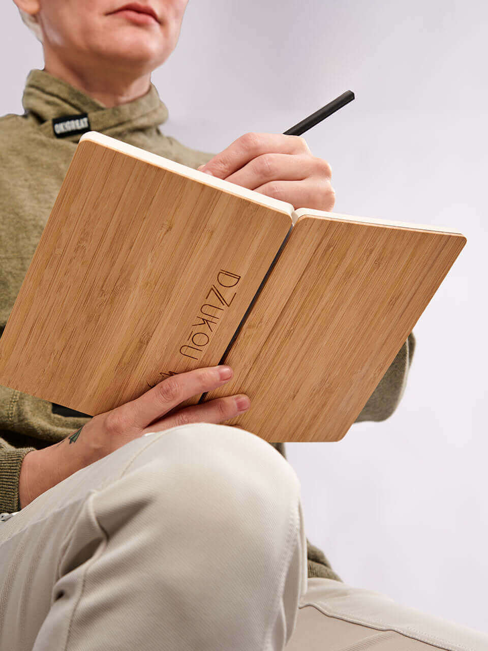 A woman seated on a chair, diligently writing in a bamboo notebook, focused on her task.