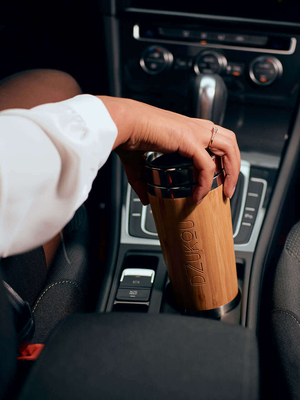 A person sitting in a car, holding a bamboo coffee tumbler, enjoying a moment of relaxation.