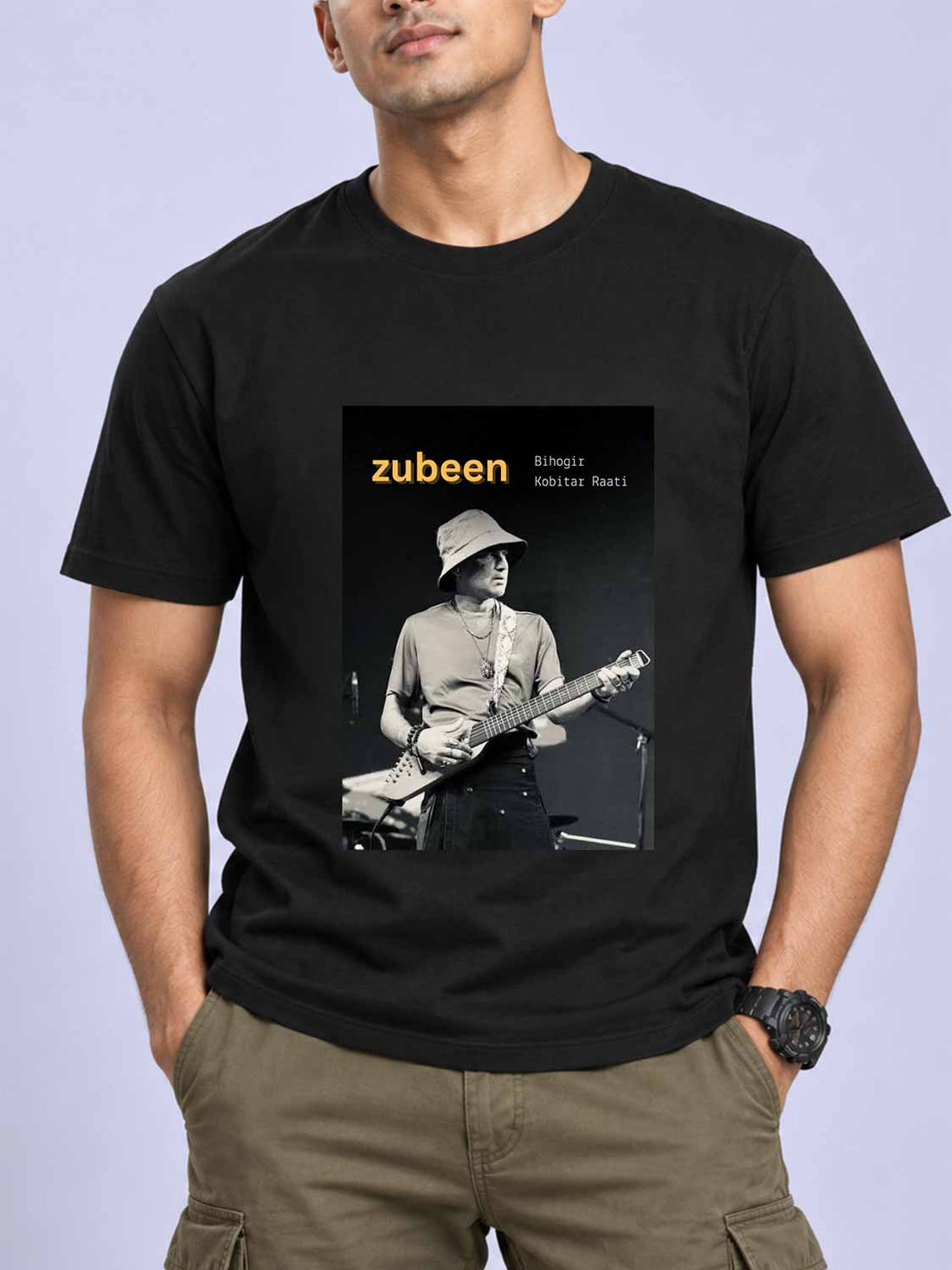 A man wearing a black short-sleeve t-shirt with a graphic print of musician Zubeen on the front, paired with khaki cargo pants, set against a light lavender background.