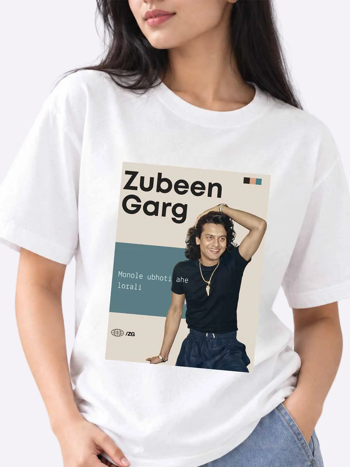 A woman wearing a white graphic T-shirt featuring a printed portrait of Zubeen Gang with text, shown against a light lavender studio background.