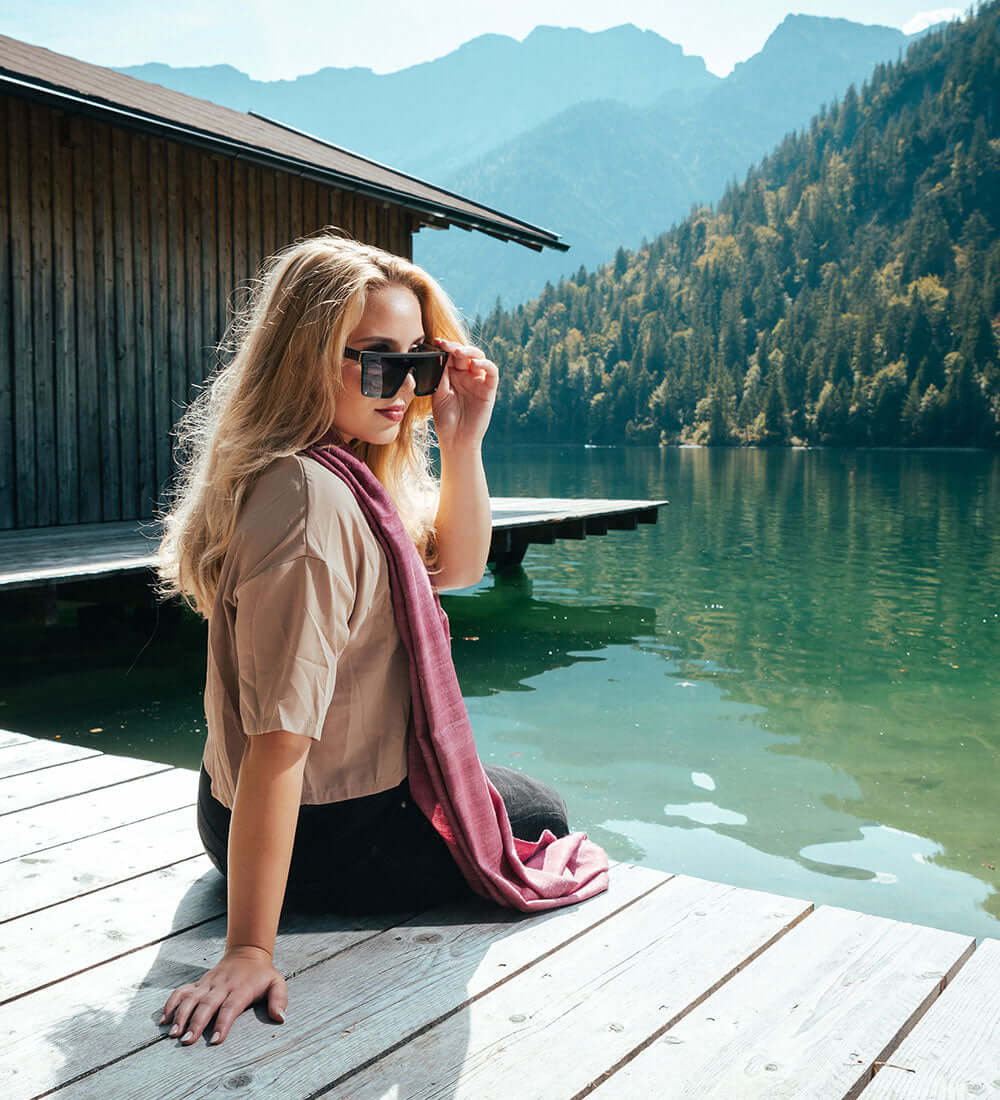 a girl sitting beside a lake wearing sunglasses and stole