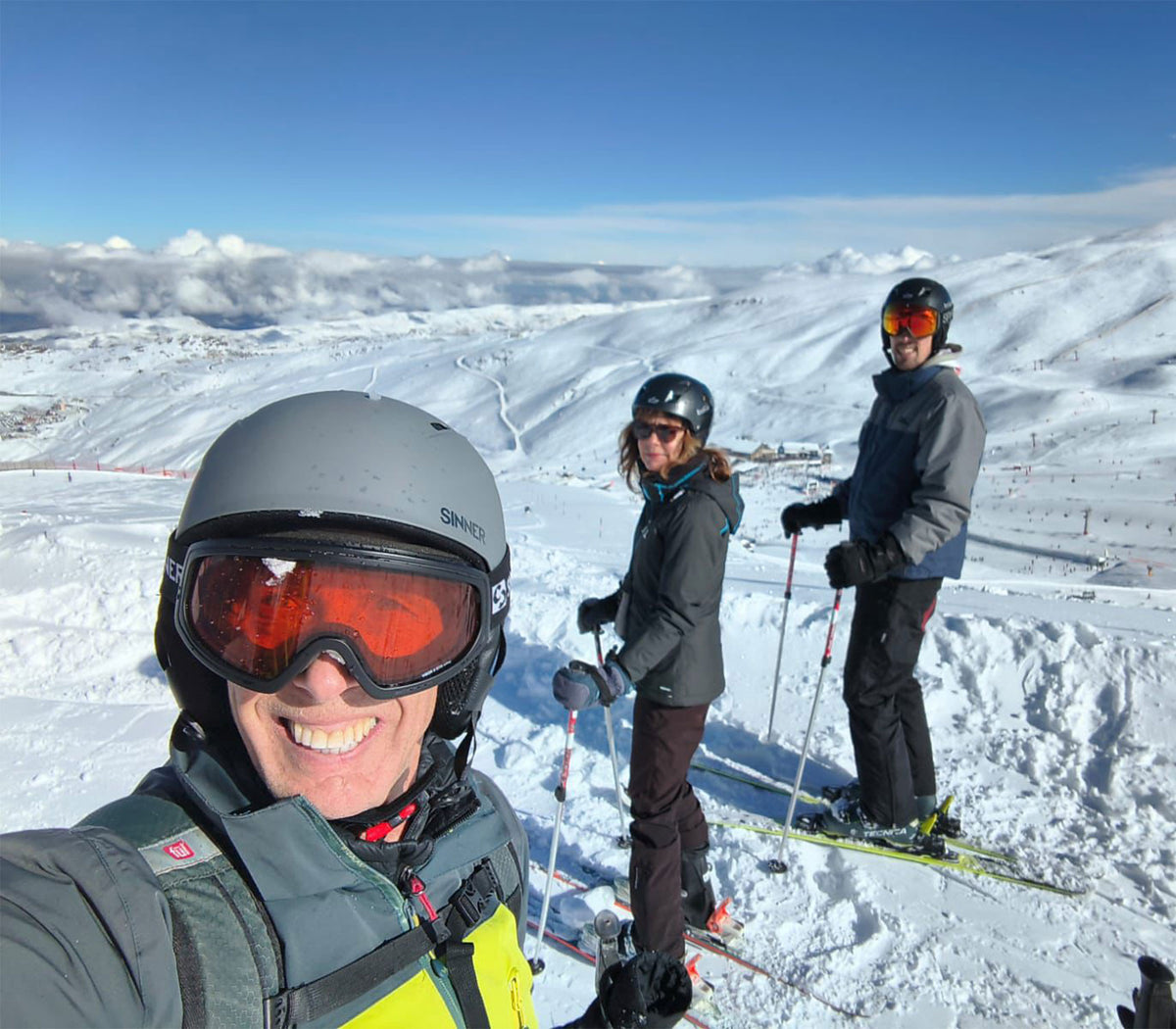 Three skiers on a snowy mountain with clear blue skies