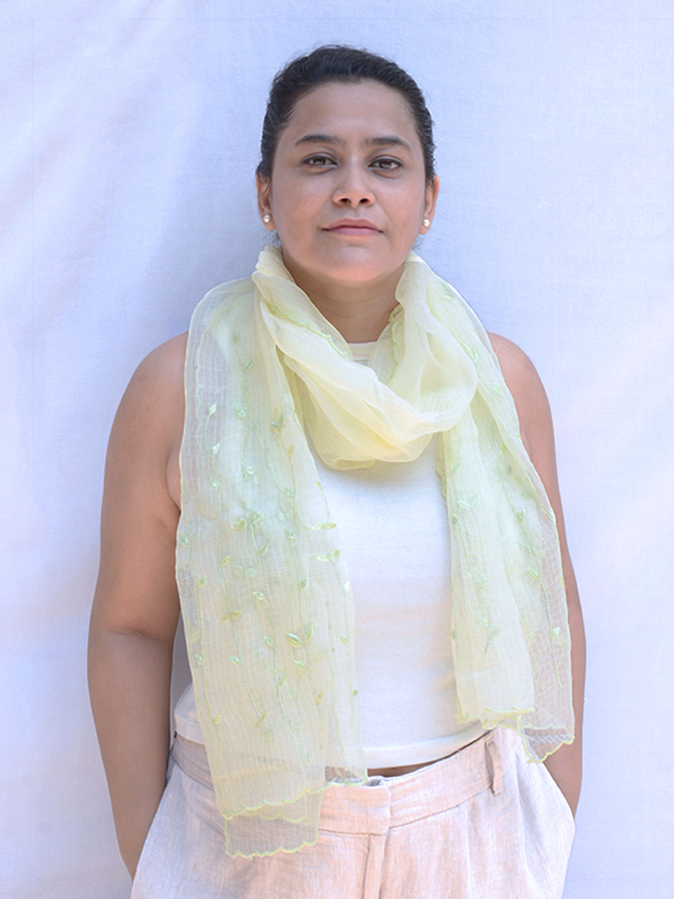 A woman in a green scarf and white tank top, smiling and enjoying a sunny day outdoors.