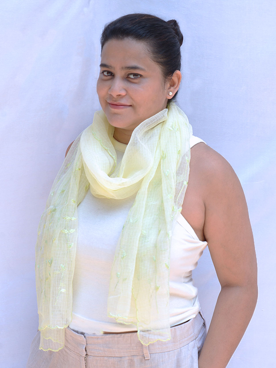 A woman in a green scarf and white tank top, smiling and enjoying a sunny day outdoors.