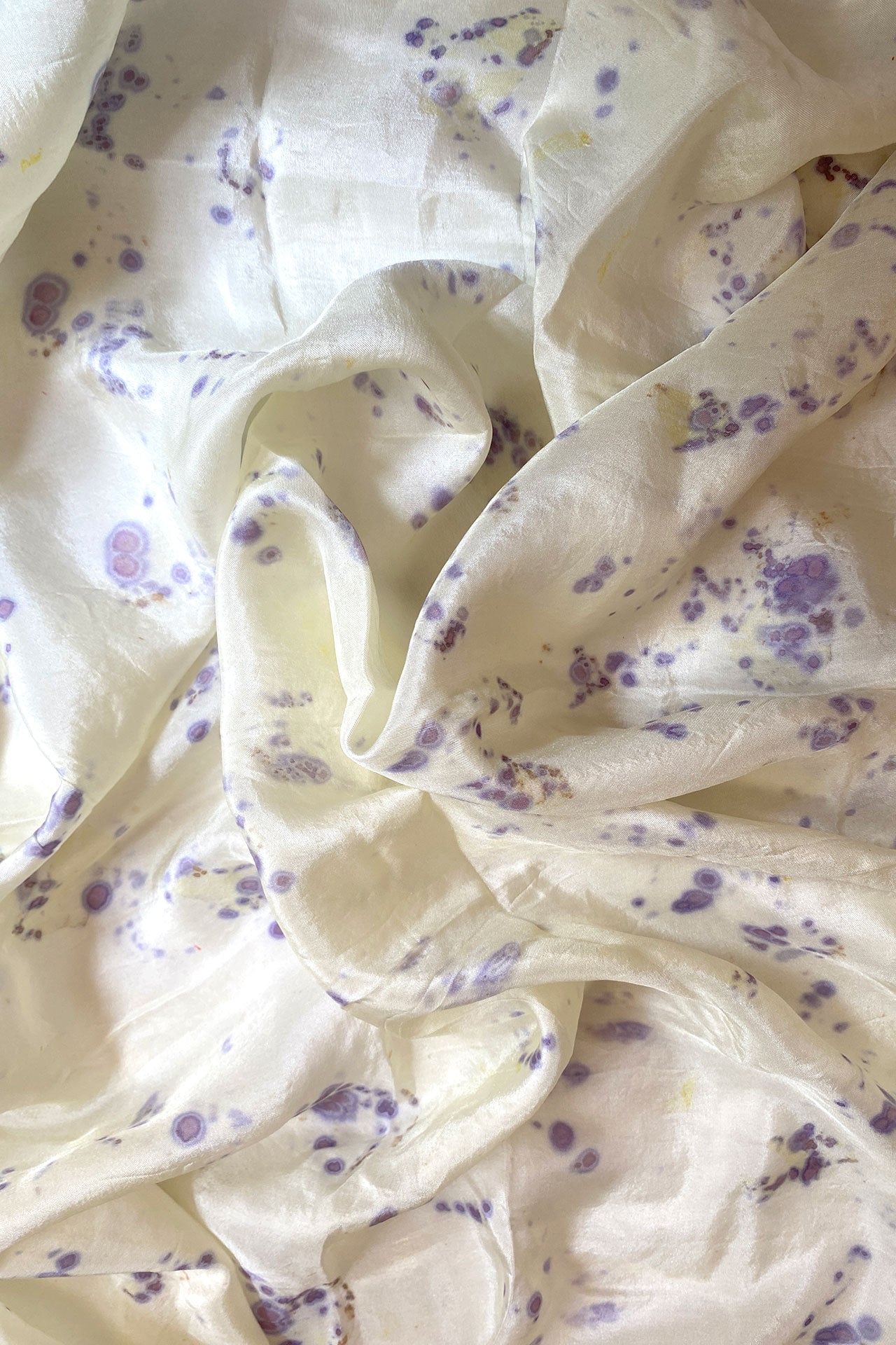 A white silk scarf adorned with delicate purple flowers, elegantly draped and showcasing its intricate design